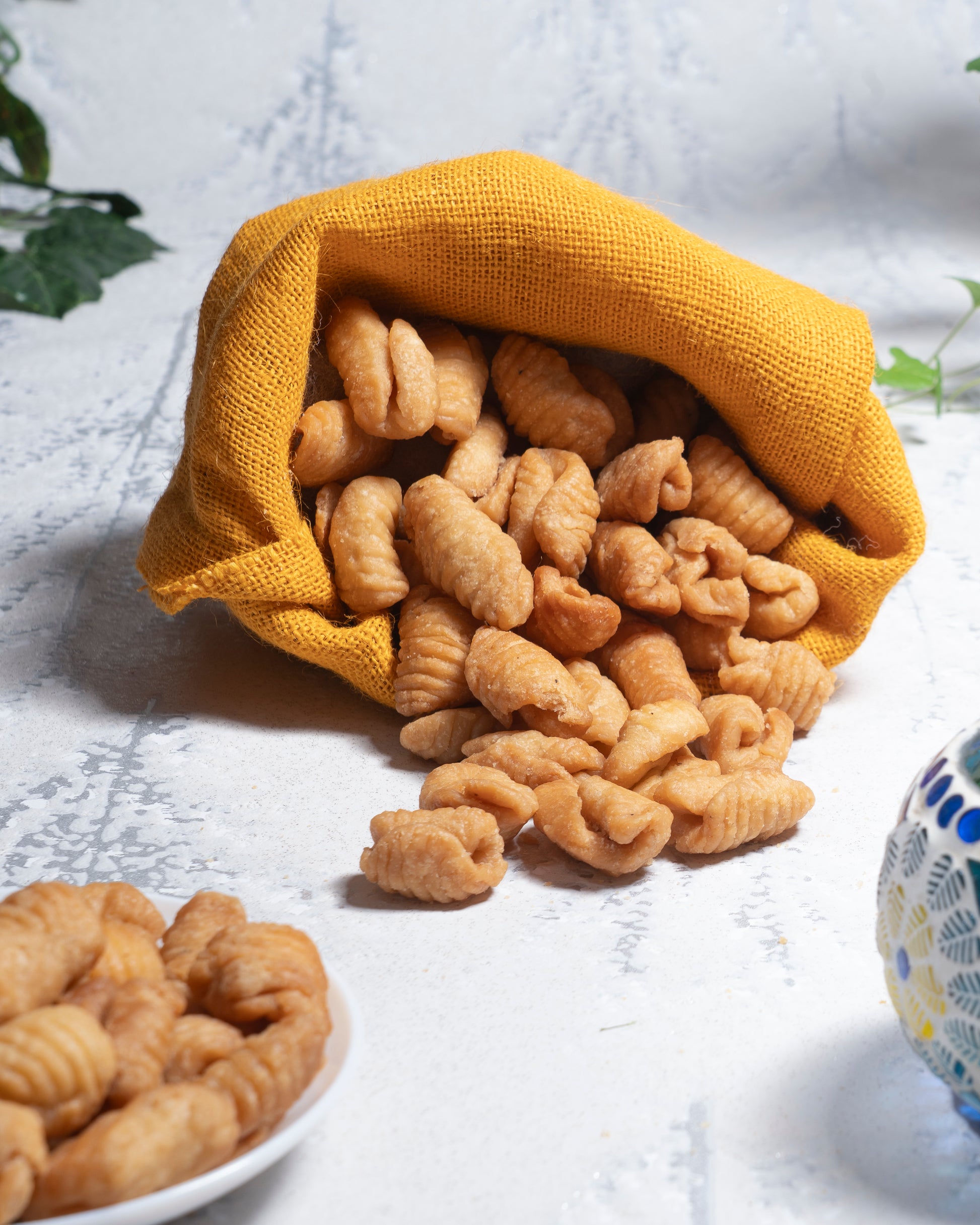 Yellow fabric bag filled with crinkled KalKal on a white surface.